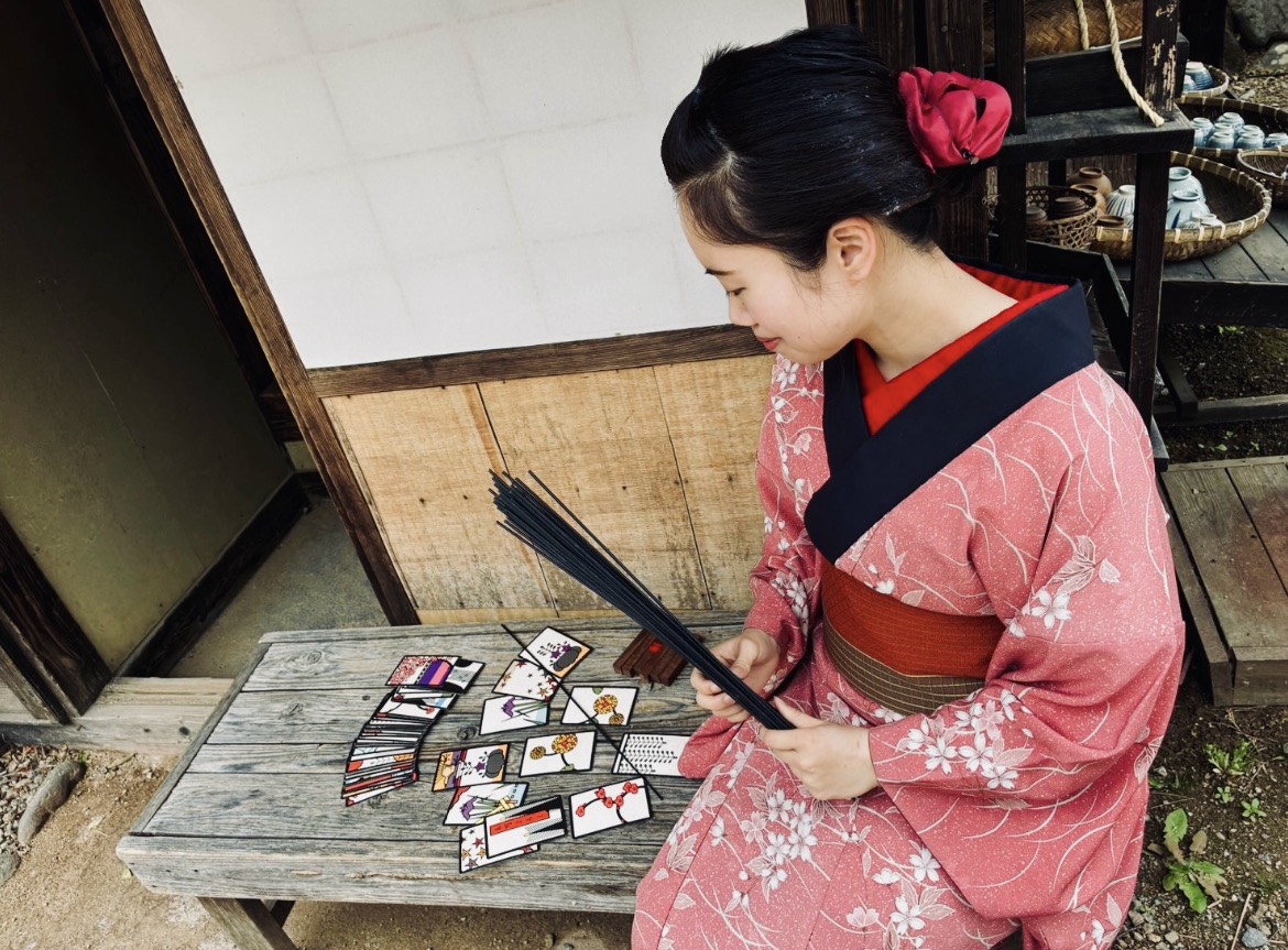 着物姿で縁台に花札を並べ、筮竹を手に読んでいるところ
